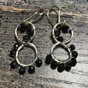 May include: A pair of dangle earrings featuring silver-toned hoops adorned with faceted black beads. The earrings have a wire-wrapped design, with a larger hoop at the bottom and a smaller one at the top, connected by a silver hook.