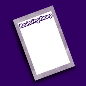 Op de afbeelding: Een wit rechthoekig notitieblok met een grijze rand en de woorden "Brain Fog Dump" in paarse tekst. Het notitieblok staat schuin op een donkerpaarse achtergrond.