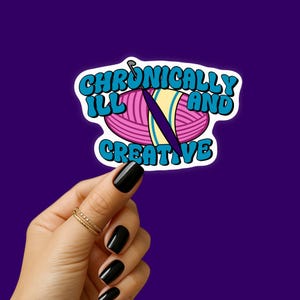 May include: A sticker with the text "Chronically Ill and Creative" in a bubble font. The design includes a pink yarn ball, a purple crochet hook, and a yellow stripe. The background is a deep purple.