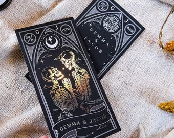 May include: Black and gold wedding invitations featuring skeleton illustrations. The invitations include the names "GEMMA & JACOB" and the date "2022". The design has a gothic theme with celestial elements.