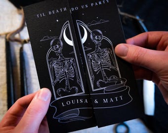 May include: Black wedding invitation with white skeleton illustration and the text "TIL DEATH DO US PARTY". The names "LOUISA & MATT" are printed on a banner. The invitation is held by a person.