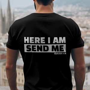 May include: Black t-shirt with the text "HERE I AM SEND ME" in white block letters. The text "ISAIAH 6:8" is below the main text. The shirt is a crew neck style.