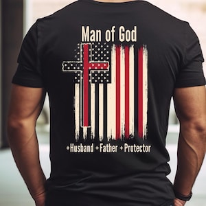 Könnte beinhalten: Schwarzes T-Shirt mit einem verblassten Design der amerikanischen Flagge und einem Kreuz. Der Text "Man of God" steht über der Flagge, und "+Husband +Father +Protector" steht darunter.