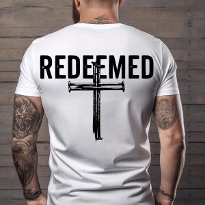 May include: White t-shirt with the word "REDEEMED" in bold black letters above a black cross design. The cross is made with nails. The shirt is plain on the front.