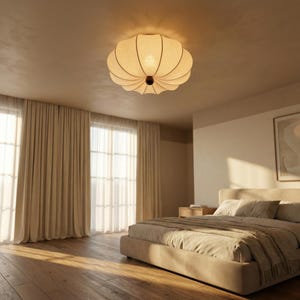 May include: A beige, fabric ceiling light fixture with a scalloped design is centered in the image. The light is circular with a dark brown centre. The room features beige curtains, a bed, and hardwood floors, creating a warm, inviting atmosphere.