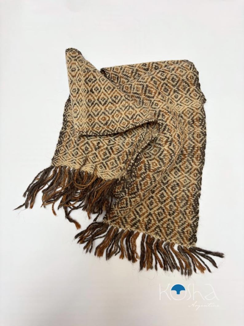 May include: A woven scarf featuring a repeating diamond pattern in shades of brown, tan, and cream. The rectangular accessory has long, loose fringe along the short edges. The bottom right corner displays the text KOSHA Argentina with a blue icon.