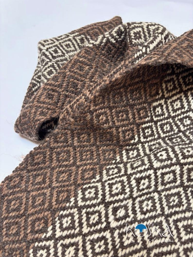 May include: A woven textile featuring a repeating geometric square pattern in shades of dark brown and cream. The fabric displays a textured, interlaced appearance with a consistent grid design throughout the material, including the logo KOSHA.
