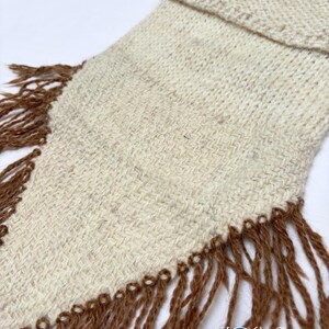 May include: A cream-coloured woven textile piece with a folded top edge and long, brown fringe detailing along the sides. The fabric features a subtle, textured weave pattern. The logo Kosha Argentina is printed in the bottom right corner.