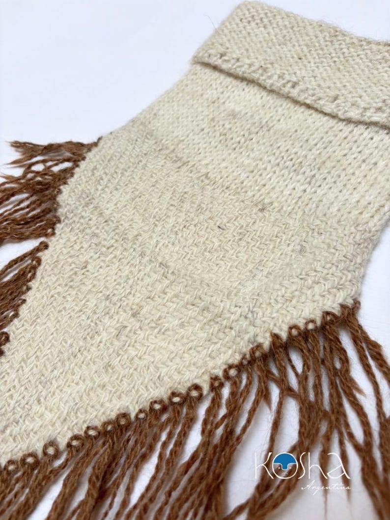 May include: A cream-coloured woven textile piece with a folded top edge and long, brown fringe detailing along the sides. The fabric features a subtle, textured weave pattern. The logo Kosha Argentina is printed in the bottom right corner.