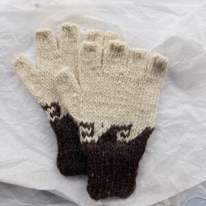 May include: A pair of fingerless gloves featuring a two-tone design with a cream-colored upper section and a dark brown ribbed cuff. The transition between the colors displays a geometric pattern, and the knit texture is visible throughout.