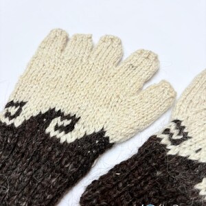 May include: A pair of fingerless gloves featuring a two-tone knit pattern in cream and dark brown. The design includes a geometric wave-like motif separating the colors. The text "Kosha Argentina" is printed in the lower right corner.
