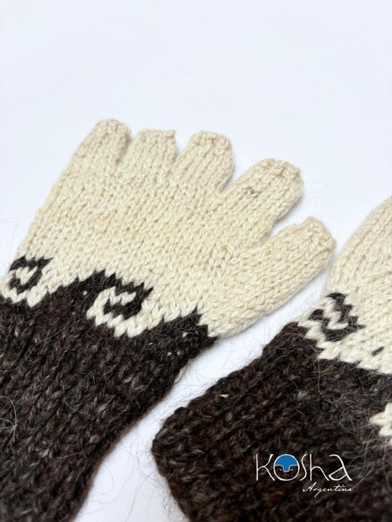 May include: A pair of fingerless gloves featuring a two-tone knit pattern in cream and dark brown. The design includes a geometric wave-like motif separating the colors. The text "Kosha Argentina" is printed in the lower right corner.
