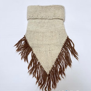 May include: A triangular-shaped neck warmer made of off-white knit fabric with a folded collar at the top. The bottom edges are adorned with long, dark brown fringe tassels. The logo "Kosha Argentina" is printed in the bottom right corner.
