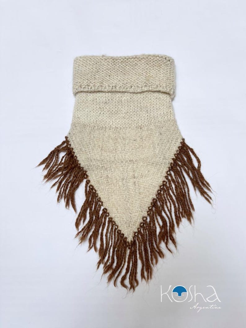 May include: A triangular-shaped neck warmer made of off-white knit fabric with a folded collar at the top. The bottom edges are adorned with long, dark brown fringe tassels. The logo "Kosha Argentina" is printed in the bottom right corner.