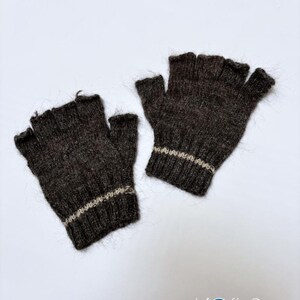 Puede incluir: Un par de guantes sin dedos hechos de un material de punto difuso de color marr&oacute;n oscuro. Cada guante presenta un pu&ntilde;o acanalado con una franja horizontal de color beige claro cerca de la mu&ntilde;eca. El texto "Kosha Argentina" aparece abajo.