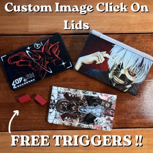 Puede incluir: Tapas de imagen personalizadas con varios diseños gráficos, incluyendo arte estilo anime y patrones abstractos. La imagen también muestra dos gatillos rojos y el texto "FREE TRIGGERS!!" sobre una superficie de madera.