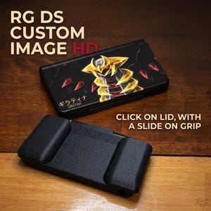 May include: A black handheld gaming console featuring a custom graphic of the yellow and black creature Giratina on the lid, with Japanese text and the name Giratina. Below it is a separate black textured slide-on grip accessory.