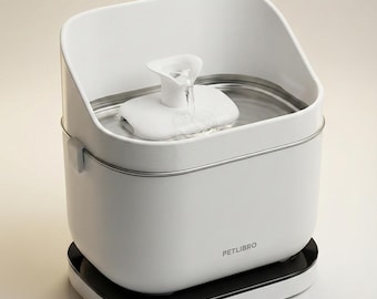 Peut inclure: Une fontaine à eau pour animaux Petlibro blanche avec un bassin en acier inoxydable et un bec verseur central blanc. L'appareil présente un corps blanc rectangulaire aux coins arrondis, posé sur une base noire. L'eau coule du bec.