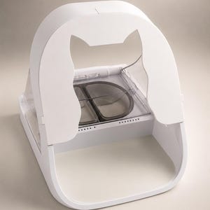 May include: A white automatic pet feeder featuring a cat-shaped silhouette cutout on the front panel. The device includes a clear plastic lid covering a dual-compartment food tray with dark gray inserts and a series of small ventilation holes.