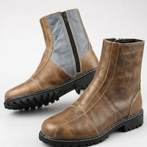May include: A pair of ankle boots featuring a tan brown finish with a smooth texture. The boots have a black side zipper, a vertical seam detail along the front, and a thick black lug sole with a deep tread pattern for traction and stability.