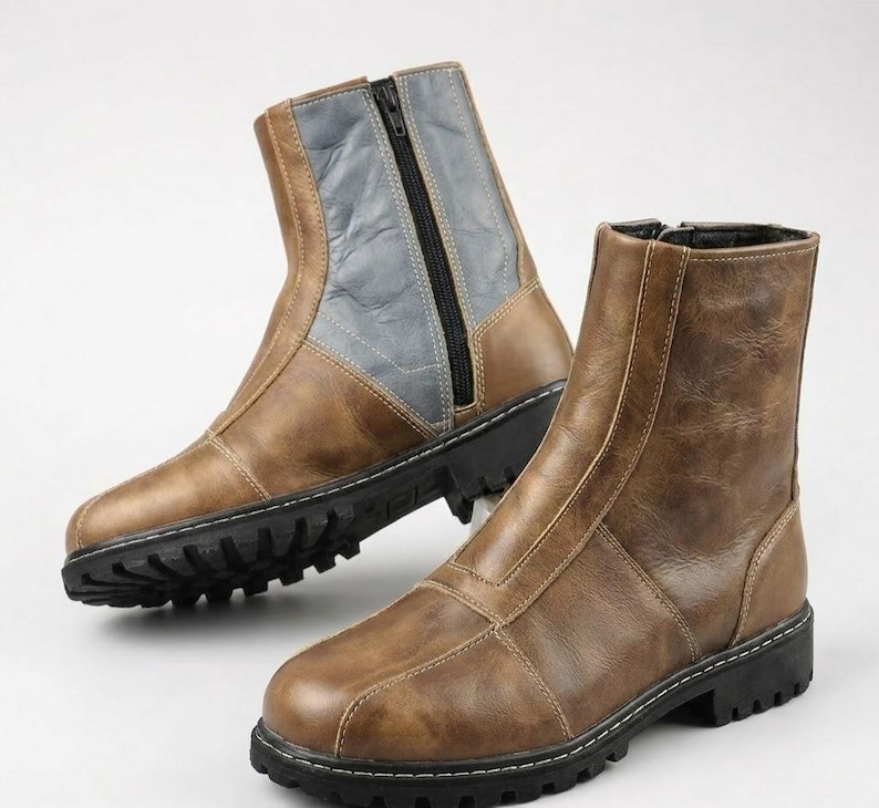 May include: A pair of ankle boots featuring a tan brown finish with a smooth texture. The boots have a black side zipper, a vertical seam detail along the front, and a thick black lug sole with a deep tread pattern for traction and stability.