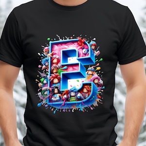 Puede incluir: Camiseta negra con un dise&ntilde;o de dibujos animados colorido de la letra "E". La letra es azul con un interior rosa, rodeada de personajes de dibujos animados y salpicaduras de pintura. Un dise&ntilde;o divertido y juguet&oacute;n.