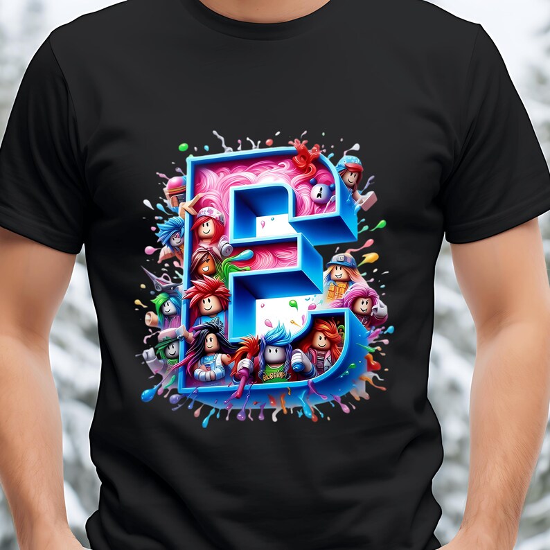 Puede incluir: Camiseta negra con un dise&ntilde;o de dibujos animados colorido de la letra "E". La letra es azul con un interior rosa, rodeada de personajes de dibujos animados y salpicaduras de pintura. Un dise&ntilde;o divertido y juguet&oacute;n.