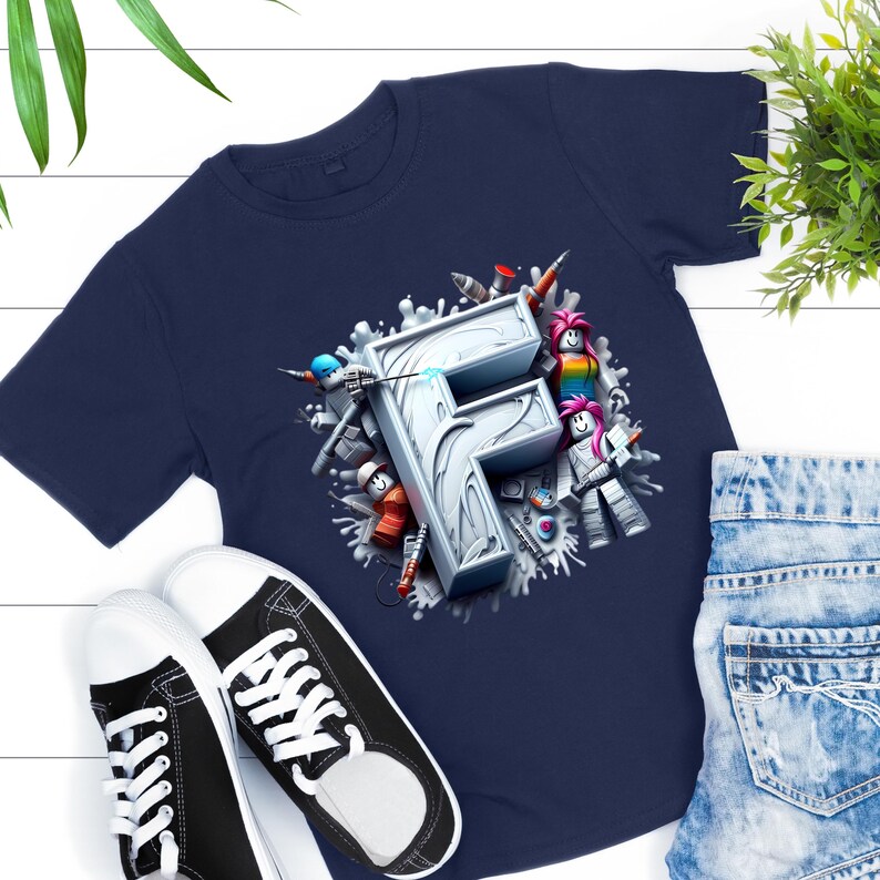 Puede incluir: Camiseta azul marino con una gran letra "F" estilizada en 3D y personajes de dibujos animados. El dise&ntilde;o incluye salpicaduras blancas y varios colores. Tambi&eacute;n se ven zapatillas deportivas blancas y negras y pantalones cortos vaqueros.