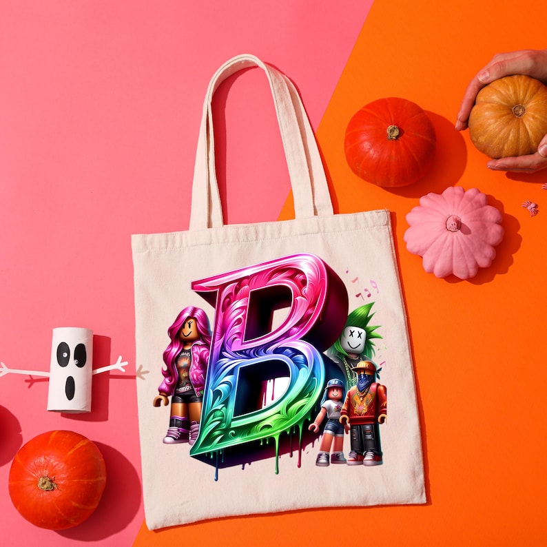 Puede incluir: Un bolso tote color crema con una gran letra "B" goteando y colorida, con personajes de dibujos animados. La imagen incluye calabazas y un fantasma de papel sobre un fondo rosa y naranja.