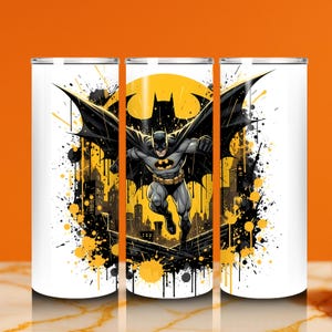 Puede incluir: Vaso blanco con un dise&ntilde;o de Batman. El dise&ntilde;o presenta a Batman en vuelo, un s&iacute;mbolo de murci&eacute;lago amarillo y una silueta de ciudad sobre un fondo amarillo. Salpicaduras de pintura negra y amarilla enmarcan la imagen.