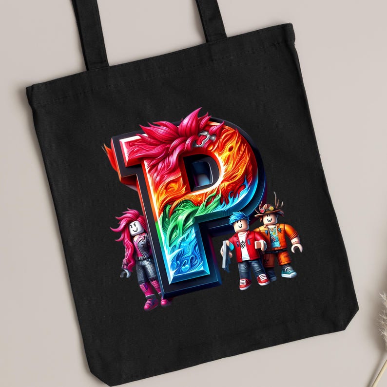 Puede incluir: Bolso tote negro con una gran letra "P" colorida en 3D. La letra est&aacute; llena de colores arco&iacute;ris y llamas. Tres figuras de dibujos animados est&aacute;n cerca de la letra. El bolso est&aacute; hecho de tela resistente.