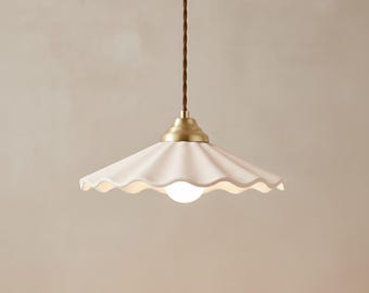 May include: A cream-coloured ceramic pendant light with a scalloped edge and a brass-coloured base. The light hangs from a brown, twisted cord. The light bulb is a small, round, white globe.