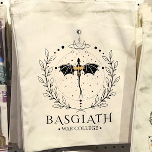 May include: Cream-coloured tote bag with a black dragon design inside a circular frame of leaves and dots. The text "BASGIATH • WAR COLLEGE •" is printed below. Other tote bags are visible in the background.