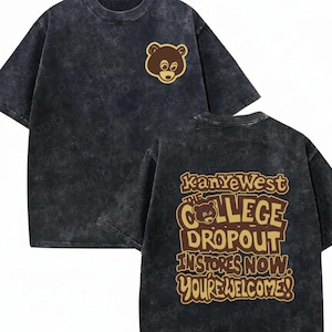 May include: A black acid-wash t-shirt featuring a small brown bear graphic on the front left chest. The back displays a large brown and tan graphic with the text Kanye West The College Dropout In Stores Now. You're Welcome! and a bear icon.