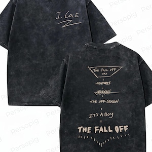May include: A black acid-wash short-sleeve t-shirt. The front features the text J. COLE in light tan. The back displays a graphic with the text THE FALL OFF ERA, FEATURES, THE OFF-SEASON, IT'S A BOY, and THE FALL OFF in light tan lettering.