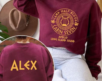 Peut inclure: Sweat-shirt bordeaux avec texte doré. L'avant présente un motif circulaire avec "CAMP HALF-BLOOD" et "CABIN SEVEN". Le dos affiche le nom "ALEX" en or. Un vêtement décontracté et confortable.
