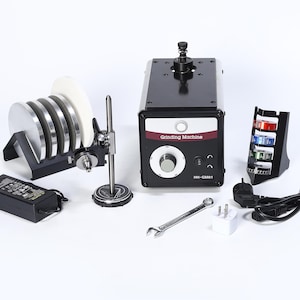 May include: A black and red grinding machine with a dial and the text "Grinding Machine". The image also shows a set of grinding wheels, a wrench, and other accessories.