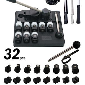 May include: A jewelry making kit with a black base, a lever, and various tools. The kit includes a ring sizer, a hammer, and multiple black and white components. The text "GEMKit" and "32 pcs" are visible.
