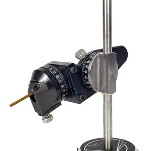 May include: A black and silver precision instrument with a vertical post and adjustable angled components. The device has a circular base with text and a dial with degree markings. A small, gold-colored rod extends from the angled section.