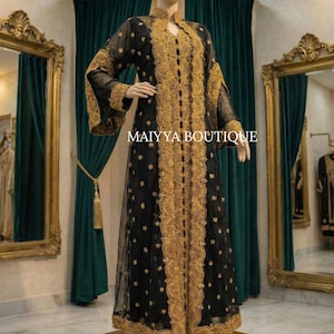 May include: A black, floor-length dress with gold embroidery and sheer sleeves is displayed on a mannequin. The dress features intricate gold detailing down the front and around the sleeves. The text "MAIYYA BOUTIQUE" is visible on the dress.