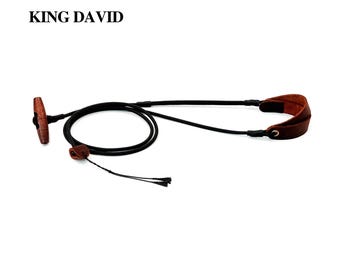 Peut inclure: Une sangle en cordon noir avec une bascule en bois marron et des accents en cuir marron. Le texte KING DAVID est imprimé en noir dans le coin supérieur gauche. La sangle présente un design en boucle avec un ajusteur en cuir et deux extrémités.