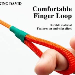 Puede incluir: Un cord&oacute;n tejido de color naranja con un conector de tubo termorretr&aacute;ctil verde y un lazo para el dedo. El texto KING DAVID, Comfortable Finger Loop y Durable material Features an anti-slip effect est&aacute; impreso sobre el fondo blanco.