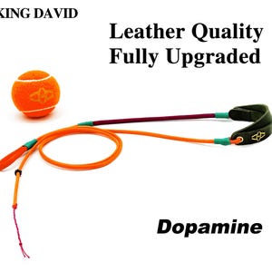 Puede incluir: Una pelota de tenis naranja con un logotipo junto a una correa de cuerda larga naranja y granate con un asa de cuero verde oscuro con un logotipo dorado. El texto dice KING DAVID, Leather Quality Fully Upgraded y Dopamine sobre fondo blanco.