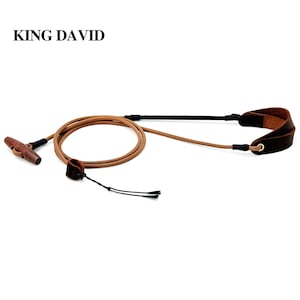 May include: A camera strap labeled KING DAVID featuring a tan cord, a dark brown leather wrist loop, and a wooden toggle fastener. The strap includes black connectors and a thin black tether cord attached to a small leather loop for secure attachment.