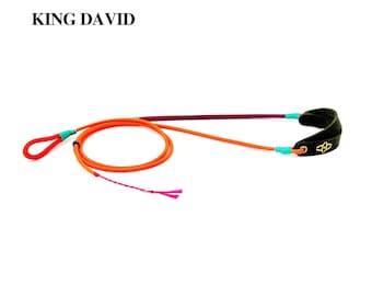 Peut inclure: Une fronde de marque King David composée d'une corde orange vif avec une poignée en boucle, une section violette et une poche en cuir noir avec un logo doré. La corde est fixée par des accents bleu clair et inclut un détail rose effiloché.