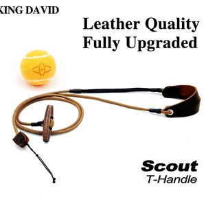 May include: A tan cord leash with a brown wooden T-handle and a dark brown leather wrist loop, accompanied by a yellow tennis ball. The text reads KING DAVID, Leather Quality Fully Upgraded, and Scout T-Handle on a white background.