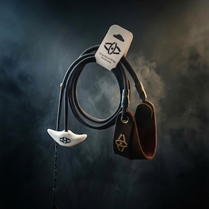 Puede incluir: Una honda de cordón negro con una lengüeta de liberación blanca moldeada y un lazo de cuero marrón para el dedo. El producto se sujeta con una etiqueta de cartón con la marca King David Sling. El diseño incluye un logotipo negro en la lengüeta.