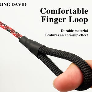 Puede incluir: Un lazo de cuerda negra para el dedo unido a una correa de cuerda con patr&oacute;n rojo y negro mediante un conector negro. El texto KING DAVID, Comfortable Finger Loop y Durable material Features an anti-slip effect aparece sobre el fondo blanco.