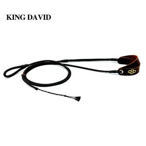 Puede incluir: Una correa de cuerda negra con un asa de cuero marrón que presenta un logotipo dorado y el texto KING DAVID. La correa incluye un anillo de metal, una cuenta deslizante y un extremo trenzado. El diseño incorpora un lazo y una cuerda larga.