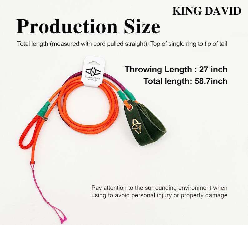 Puede incluir: Una honda hecha a mano King David con cuerda naranja, un lazo de cuero verde oscuro para el dedo con un logo dorado y una cola rosa. El texto indica una longitud de lanzamiento de 68,58 cm y una longitud total de 149,1 cm. Incluye una etiqueta.